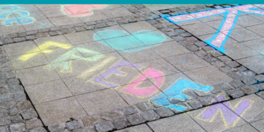 Der Schriftzug Frieden in bunt und auf Asphalt.