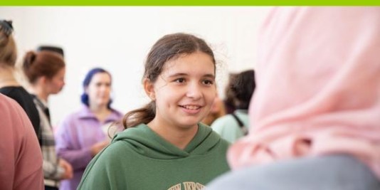 Ein lächelndes Mädchen mit brauen Haaren im Gespräch.