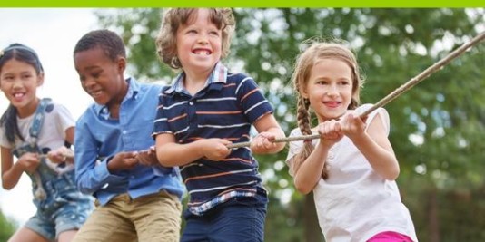 Vier Kinder stehen hintereinander und ziehen lachend an einem Seil.